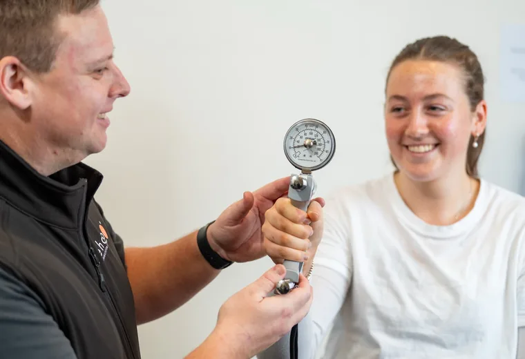 A Rehab Co clinician measuring grip strength with a hand dynamometer